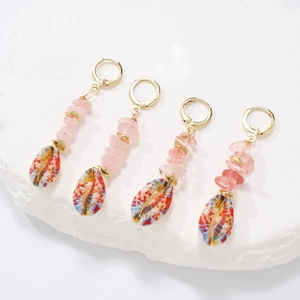 Detail of bohemian drop earrings with pink stones and painted shells on white stone display