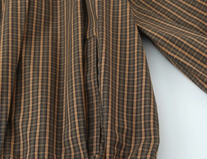 Detailed macro view of the stitching and brown plaid pattern on a cotton shirt