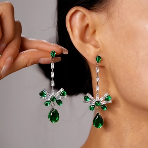 Close-up of emerald green zircon bow drop earrings worn on a model's ear