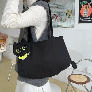 Detail of cute cat canvas tote bag with yellow embroidery and 3D tail in a cafe setting