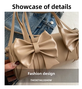 Close-up of beige cylindrical handbag featuring two large decorative 3D bows and slim strap