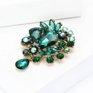 Vintage floral green crystal brooch pin with antique gold plating on a geometric display