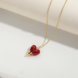 Detail of red enamel heart pendant with golden chain on white geometric background
