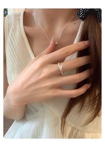 Detail of silver bow ring and star necklace set worn by a model in a lifestyle setting
