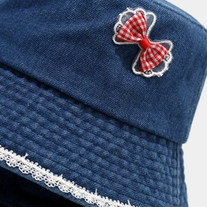 Detail of blue denim bucket hat featuring red checkered bow and white lace trim