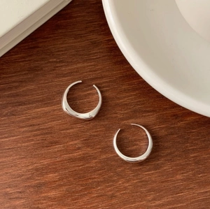Minimalist silver-plated C-shaped hoop earrings resting on a rustic wooden texture