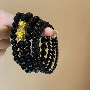 Close-up of black obsidian beaded bracelets featuring gold Pi Xiu and mantra engravings