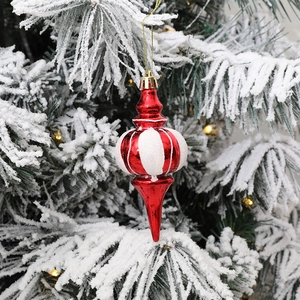 Rot-weißer Weihnachtsanhänger in Kürbisform am verschneiten Kiefernzweig mit warmem Licht