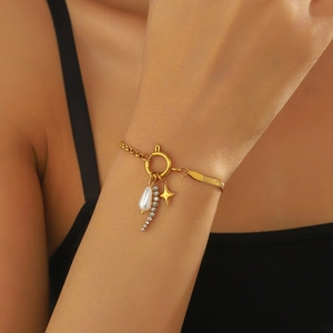 Detail of gold bracelet with asymmetric chains, pearl drop, and star charm on wrist