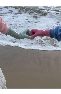 Close-up of green and pink wool knit gloves worn by a couple holding hands on a sandy beach