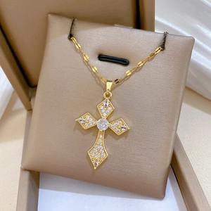 Elegant gold cross pendant necklace with sparkling crystals on a beige jewelry cushion