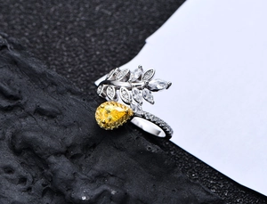 Macro shot of leaf design ring with yellow pear-cut gemstone on black rock surface