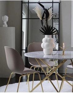 Detail view of round marble dining table with golden legs and modern taupe chairs