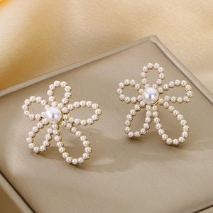 Close-up of golden hollow flower earrings with pearls on champagne silk background