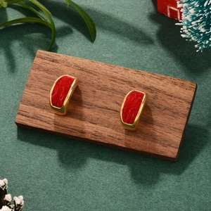 Detail of gold C-shaped earrings with red textured inlay on a dark wooden display