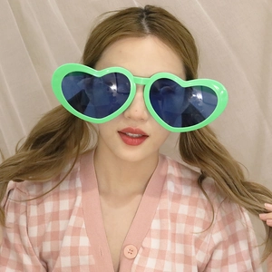 Close-up of bright green heart-shaped party sunglasses with dark blue lenses on a model