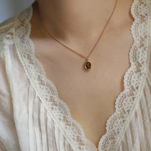 Detail of tiger eye stone coffee bean pendant on golden chain worn with lace outfit