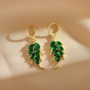 Detail view of gold earrings featuring green leaf-shaped crystals on elegant silk background