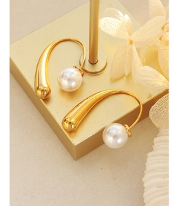 Macro detail of gold-plated geometric ear hook with white pearl on display stand