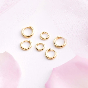 Detailed view of three different sized 18K gold plated hoop earrings on pink petals