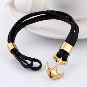 Macro shot of black braided leather bracelet featuring a gold anchor charm on white ceramic