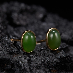 Macro shot of oval green jade stud earrings with S925 silver gold-plated base on rock