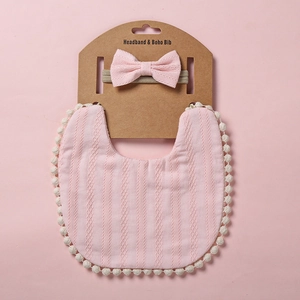 Détail du bavoir rose avec pompons blancs et bandeau à nœud assorti pour bébé