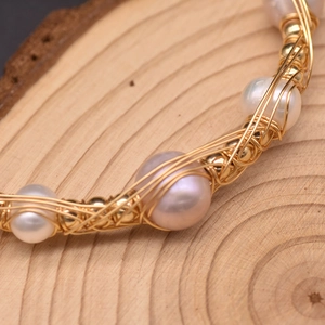 Handcrafted gold wire wrapped freshwater pearl bracelet on a rustic wood background