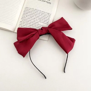 Detail view of a large red satin bow headband on an open book over white background