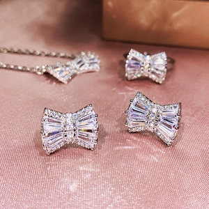 Detailed view of silver bow jewelry set with sparkling zircon stones on pink silk fabric
