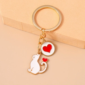Close-up of golden metal keychain featuring white cat and red enamel heart charms