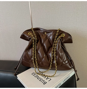 Close-up of quilted brown leather bucket bag with gold chain strap on a sofa