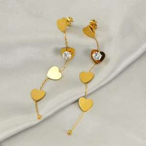 Golden heart drop earrings with zircon crystals on a luxury satin background