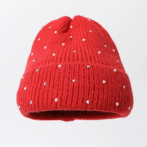 Détail du bonnet rouge en tricot avec des perles blanches et des strass argentés