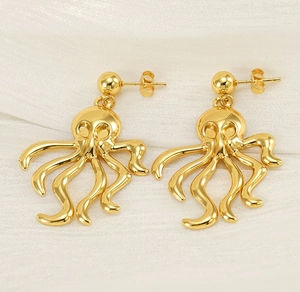 Macro detail of artistic gold octopus earrings on a white silk texture background