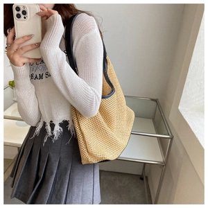 Close-up of beige woven tote bag with black shoulder straps shown on a model