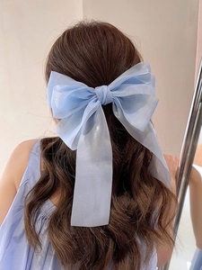 Detail of light blue organza bow hair clip with ribbons on brown wavy hair