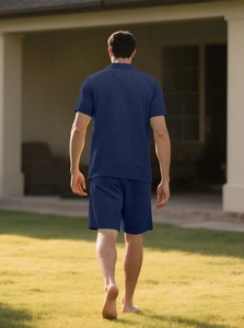 Back view of a man walking outdoors wearing a dark blue knit short sleeve shirt and shorts set