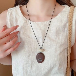 Detail of vintage wooden Saturn pendant necklace worn on white linen clothing
