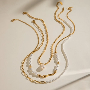 Layered gold stainless steel necklace with white freshwater pearls on a neutral background