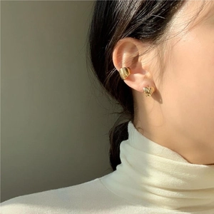 Close-up of golden heart stud and polished ear cuff worn on model with white sweater