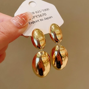 Macro view of double-layered oval earrings in polished gold-plated silver on white card