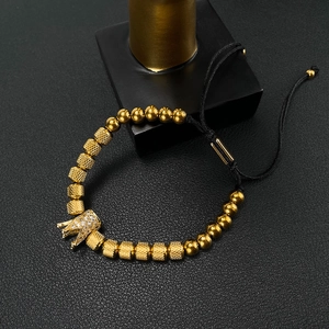 Detailed close-up of a gold crown charm bead with zircon on a braided adjustable bracelet