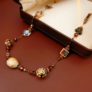 Dettaglio macro della collana lunga bohémien con perline, farfalla di vetro e ceramica