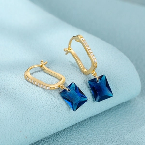 Close-up of gold U-shaped earrings with rectangular blue gemstones and micro-pave crystals