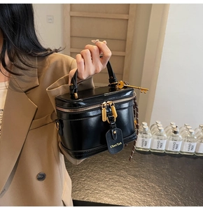 Detail of black cylindrical box bag featuring golden dual zippers and leather hangtag
