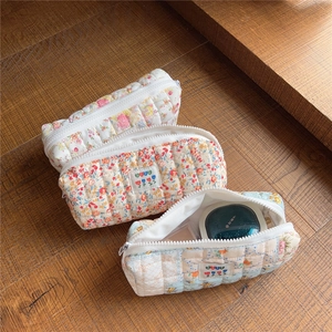 Three floral quilted cotton makeup bags with white resin zippers on a wooden surface