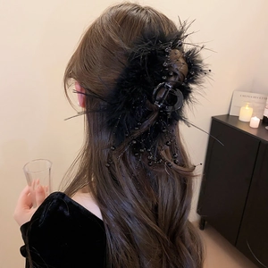 Detail of a large black feather claw clip with beaded tassels worn on a woman's long hair
