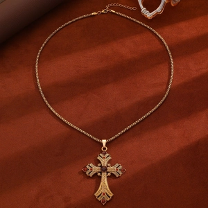 Detail of vintage gold cross necklace with red gemstones and intricate floral engravings