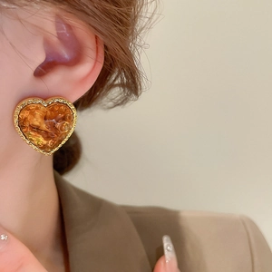 Close-up of heart-shaped amber resin earring with gold trim worn by a model